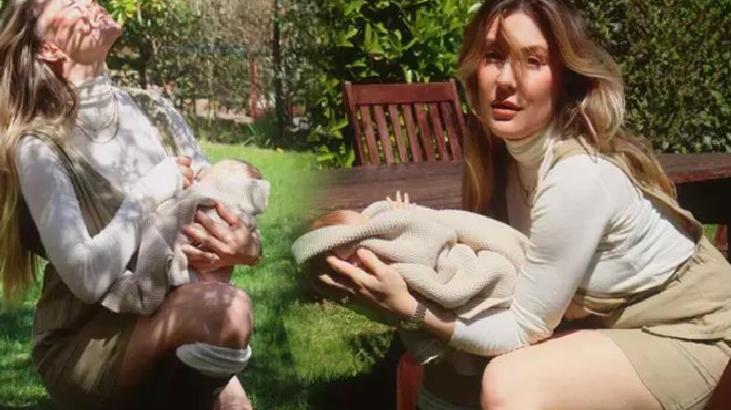 Two women outdoors holding babies wrapped in blankets in a sunny garden setting.