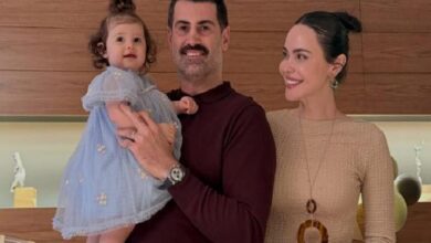 Man holds a baby girl in a blue dress while a smiling woman stands beside them in a modern kitchen.