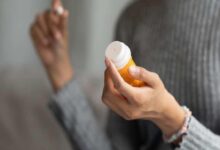Person holds an orange pill bottle with a white cap, about to pour medication into their hand or palm