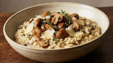 Creamy mushroom risotto topped with sautéed mushrooms, thyme sprigs, and Parmesan shavings in a rustic bowl.
