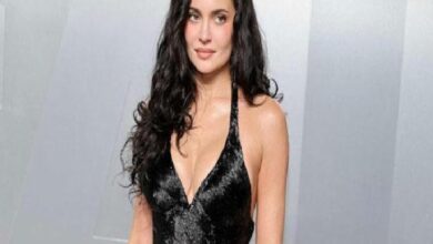 Woman with long dark hair wearing a black sequined halter dress with a plunging neckline, posing for a photo.