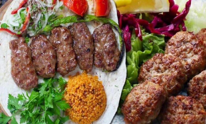 Plate with grilled kofta kebabs on flatbread, fresh herbs, and orange bulgur; crispy fried meat croquettes on greens nearby.