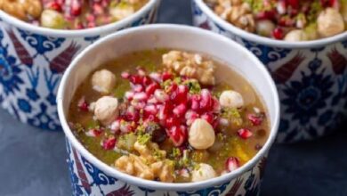 Warm spiced soup topped with pomegranate seeds, chickpeas, and nuts in a patterned ceramic bowl.