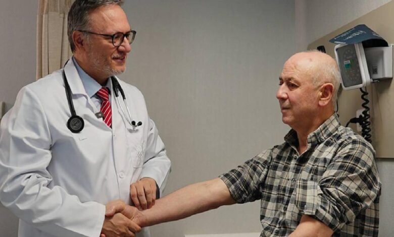 doctor in white coat shaking hands with a seated patient in a clinic examination room, both smiling, medical equipment visible in the background