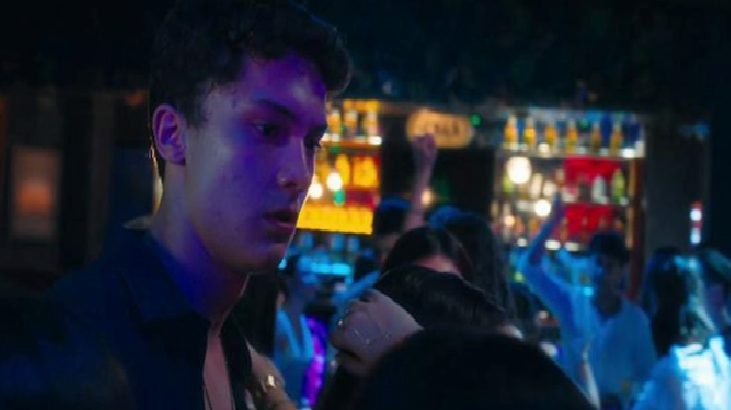 Young man in a dark shirt at a crowded bar under blue and purple lights.