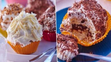 Two cupcakes with swirled frosting: white buttercream in an orange liner on a white plate, plus a bitten chocolate cupcake with chocolate shavings on a blue plate beside it.