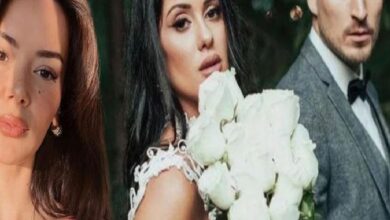 Three adults posing for a wedding photo: a woman with brown hair on the left, a bride in a white lace dress holding a large white bouquet in the center, and a man in a gray suit on the right.