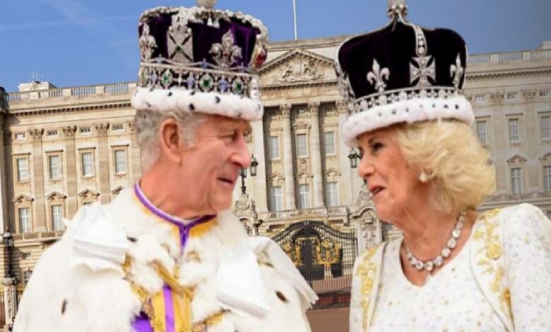 Two older adults in royal costumes and crown-like hats chat in front of a grand palace facade.