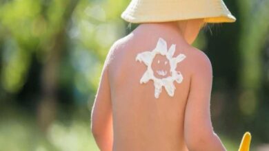 Child seen from behind wearing a straw hat; sun-shaped white sunscreen drawing on their upper back.