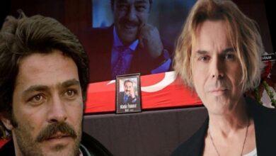 Two men stand beside a memorial display: a framed photo of a man sits in front of a Turkish flag backdrop and a large screen in the background.