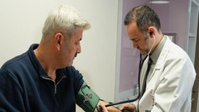 Doctor in white coat and stethoscope checks a patient's blood pressure with a cuff on his arm in a clinical room