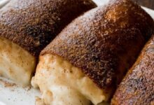 Three cinnamon-sugar coated cream-filled pastries on a plate, with melted vanilla cream oozing from the centers