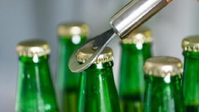 Close-up of a bottle capper applying a metal cap to green glass beer bottles during bottling