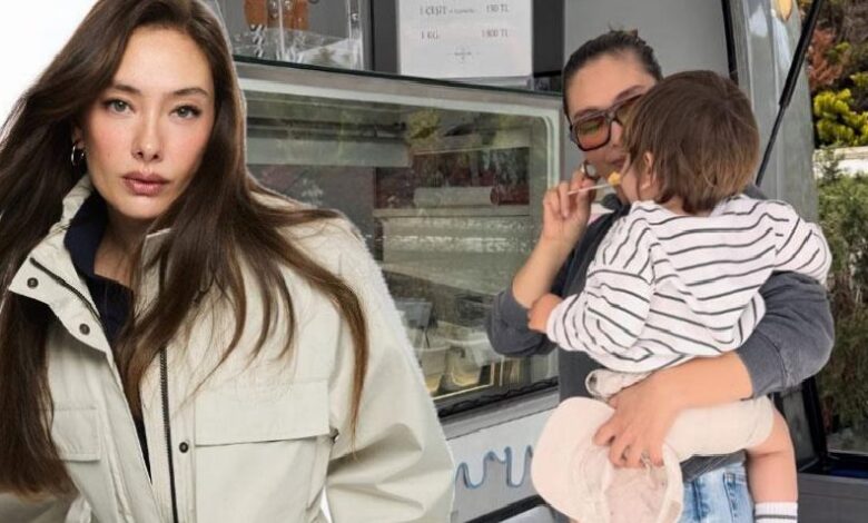 Woman with long brown hair wearing a beige jacket stands beside a food truck while another woman holds a striped-clothes toddler.