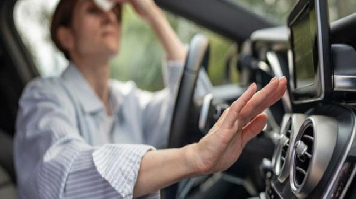 Driver resting one hand on the dashboard/center console while looking ahead inside a car. The background is slightly blurred, focusing on the dashboard controls.