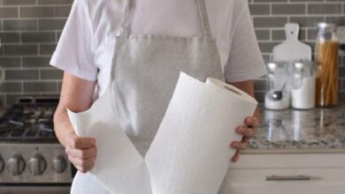 Person wearing a white shirt and gray apron holds a roll of paper towels in a kitchen