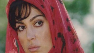 Close-up of a woman wearing a red headscarf with black dots, looking to the left outdoors.