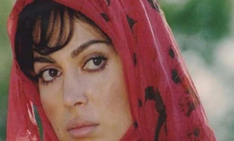 Close-up of a woman wearing a red headscarf with black dots, looking to the left outdoors.