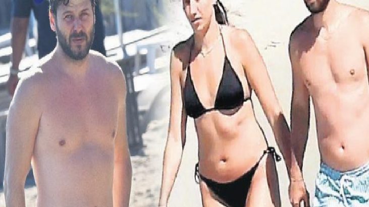Three adults in swimsuits walk along a sunny beach: a bearded man, a woman in a black bikini, and a shirtless man on the right.
