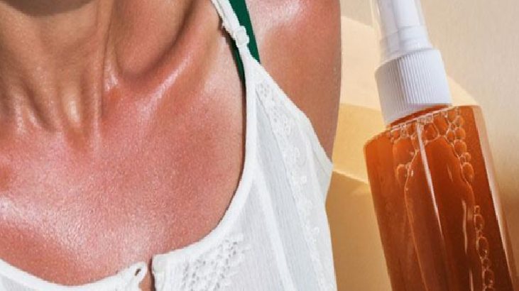 Close-up of a person’s chest area in a white top beside a spray bottle of orange liquid.