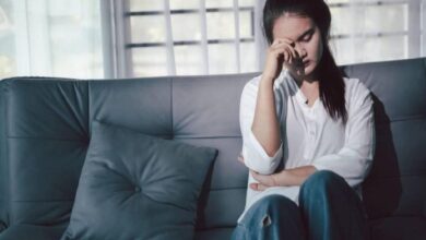 Woman sitting on a sofa with her hand over her face, looking distressed.