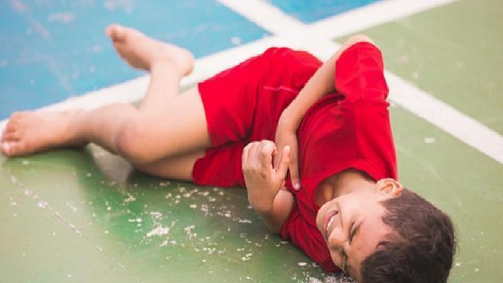 Young boy in a red shirt lying on a green and blue gym court, smiling as he rests on the floor.