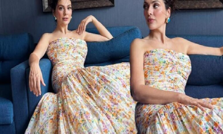 Two women in matching strapless floral dresses sit on a blue sofa, posing gracefully.