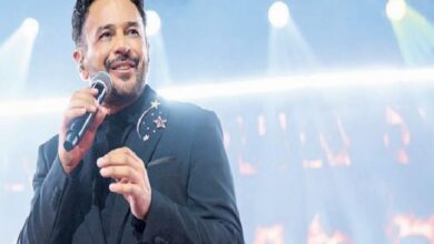 Male singer performing on a bright stage, holding a microphone and wearing a dark suit with star pins.