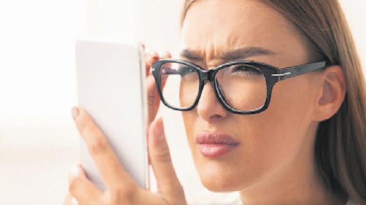 Woman wearing black-framed glasses looking intently at a smartphone held close to her face, with a puzzled expression