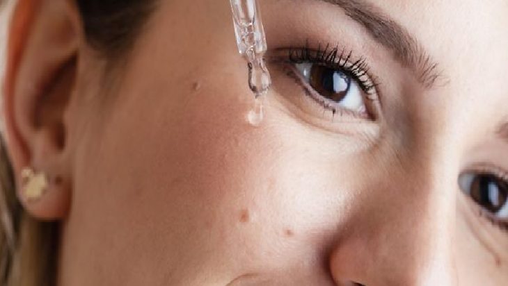 Close-up of a person applying a skincare serum with a dropper near their cheek/eye area.