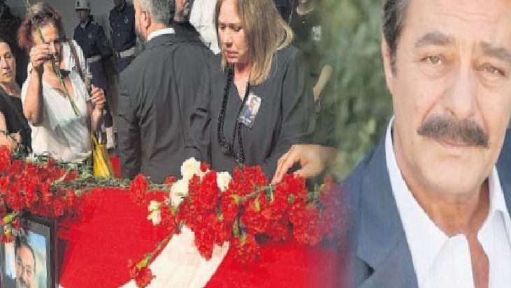 Mourners at a funeral with red flower arrangements and a framed photo; a photographer is in the background.