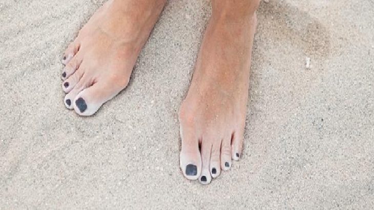 Feet with dark toenail polish resting on sandy beach.
