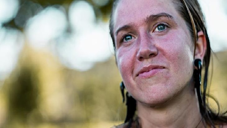 Close-up of a woman outdoors with flushed cheeks, wet hair, and blue eyes looking slightly upward.