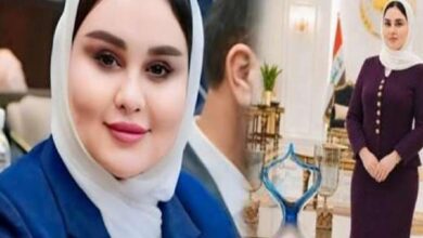Close-up of a smiling woman in a white hijab and blue blazer indoors.