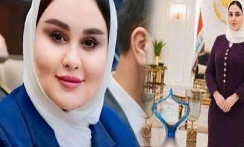 Close-up of a smiling woman in a white hijab and blue blazer indoors.