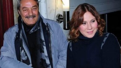 Two people sitting together, a man in a light blue jacket and scarf and a woman in a black turtleneck, smiling.