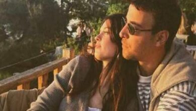 Couple leaning on a wooden railing at sunset, gazing into the distance, wearing sunglasses.