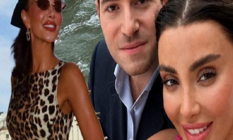 Three adults pose for a selfie outdoors by the water: a woman in a leopard print dress on the left, a man in a suit center, and a woman in pink on the right.