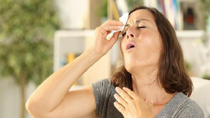 Woman with a tissue to her nose, eyes closed, appearing to sneeze or blow her nose in a home setting