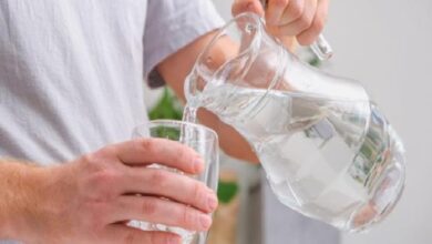 Person pouring water from a glass pitcher into a drinking glass held in the other hand