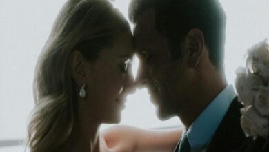 Close-up of a couple leaning foreheads together, smiling, with a bouquet visible in the background.
