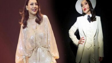 Two women on stage in glamorous outfits: one in a beige sequined dress, the other in a white suit with a hat and red lipstick.